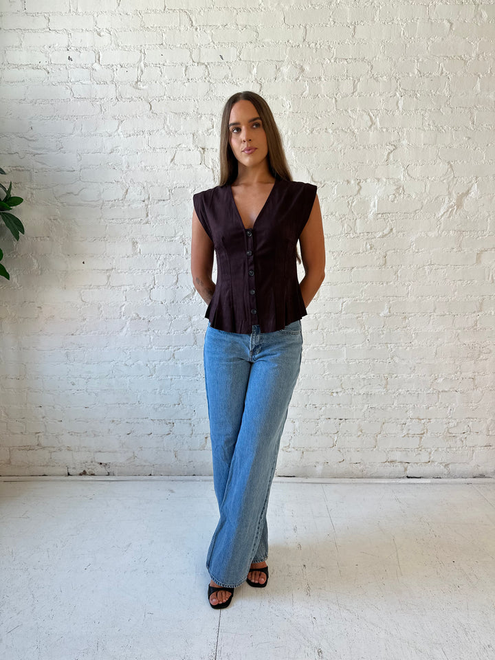 Woman wearing dark brown suede pleated peplum top with medium wash jeans. 