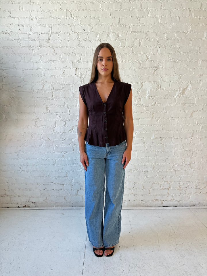 Woman wearing dark brown suede pleated peplum top with medium wash jeans. 