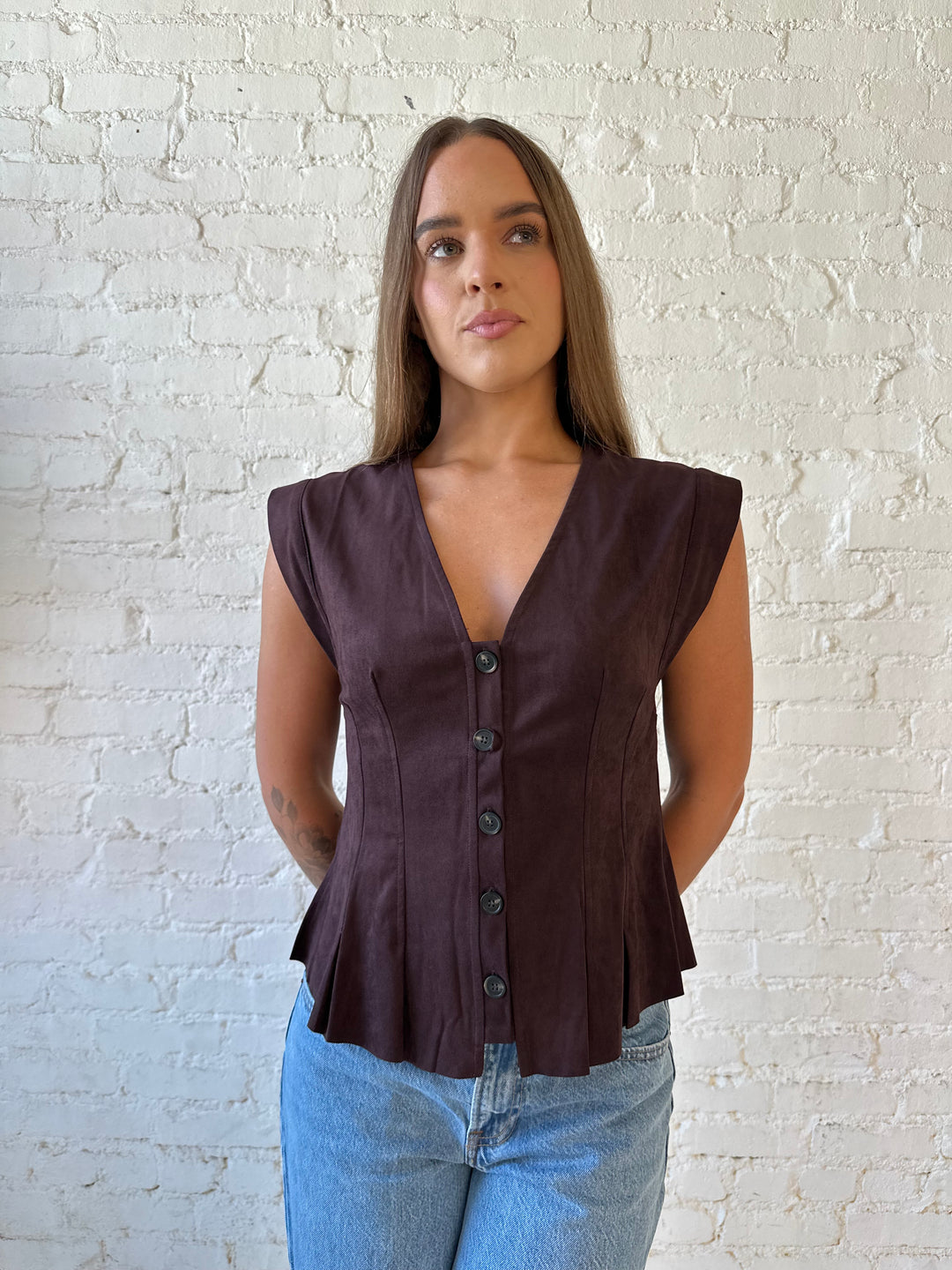 Woman wearing dark brown suede pleated peplum top with medium wash jeans. 
