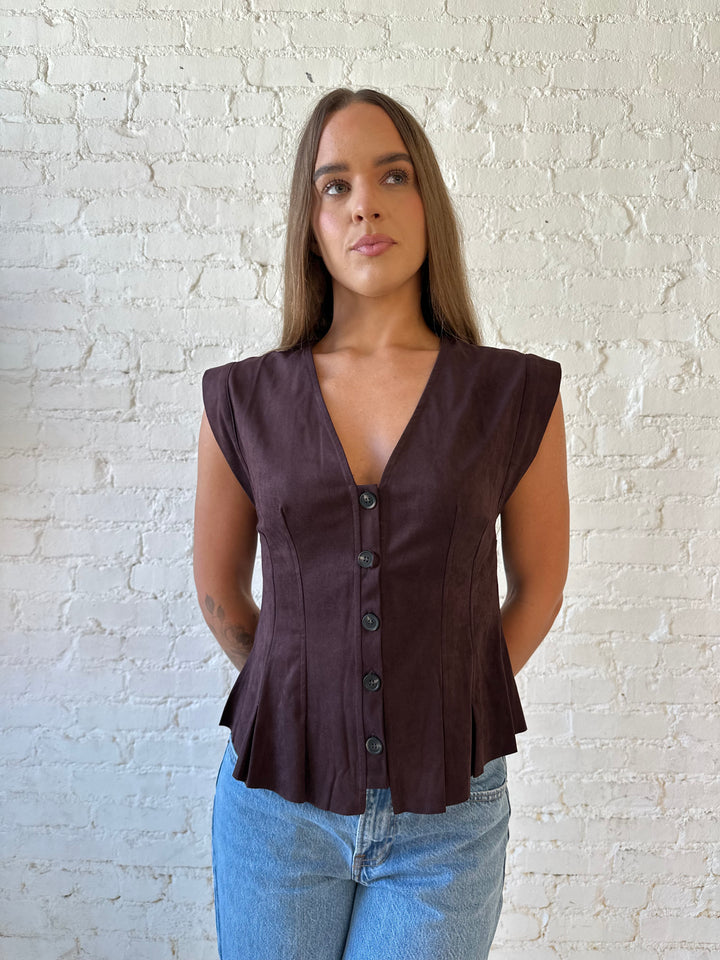 Woman wearing dark brown suede pleated peplum top with medium wash jeans. 