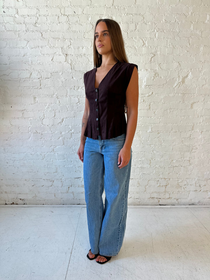 Woman wearing dark brown suede pleated peplum top with medium wash jeans. 