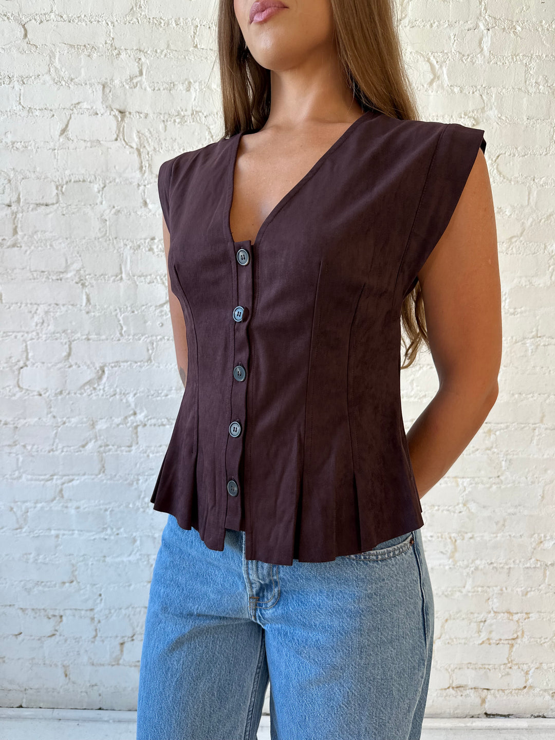 Woman wearing dark brown suede pleated peplum top with medium wash jeans. 