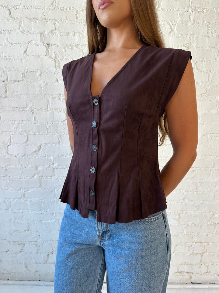 Woman wearing dark brown suede pleated peplum top with medium wash jeans. 
