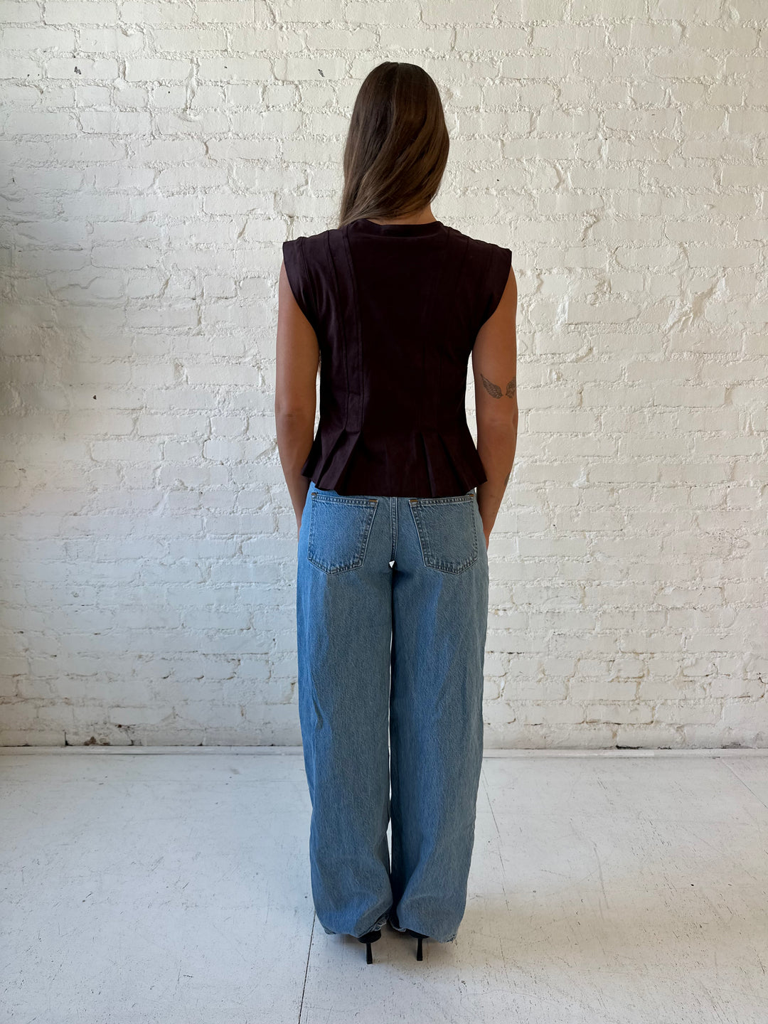 Woman wearing dark brown suede pleated peplum top with medium wash jeans. 