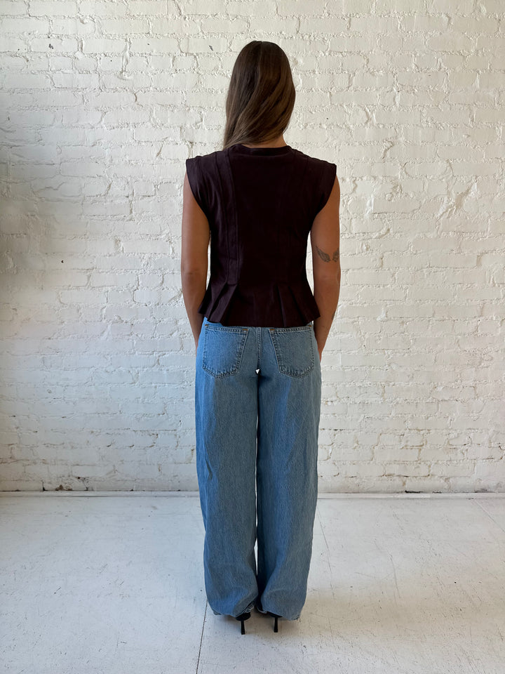 Woman wearing dark brown suede pleated peplum top with medium wash jeans. 