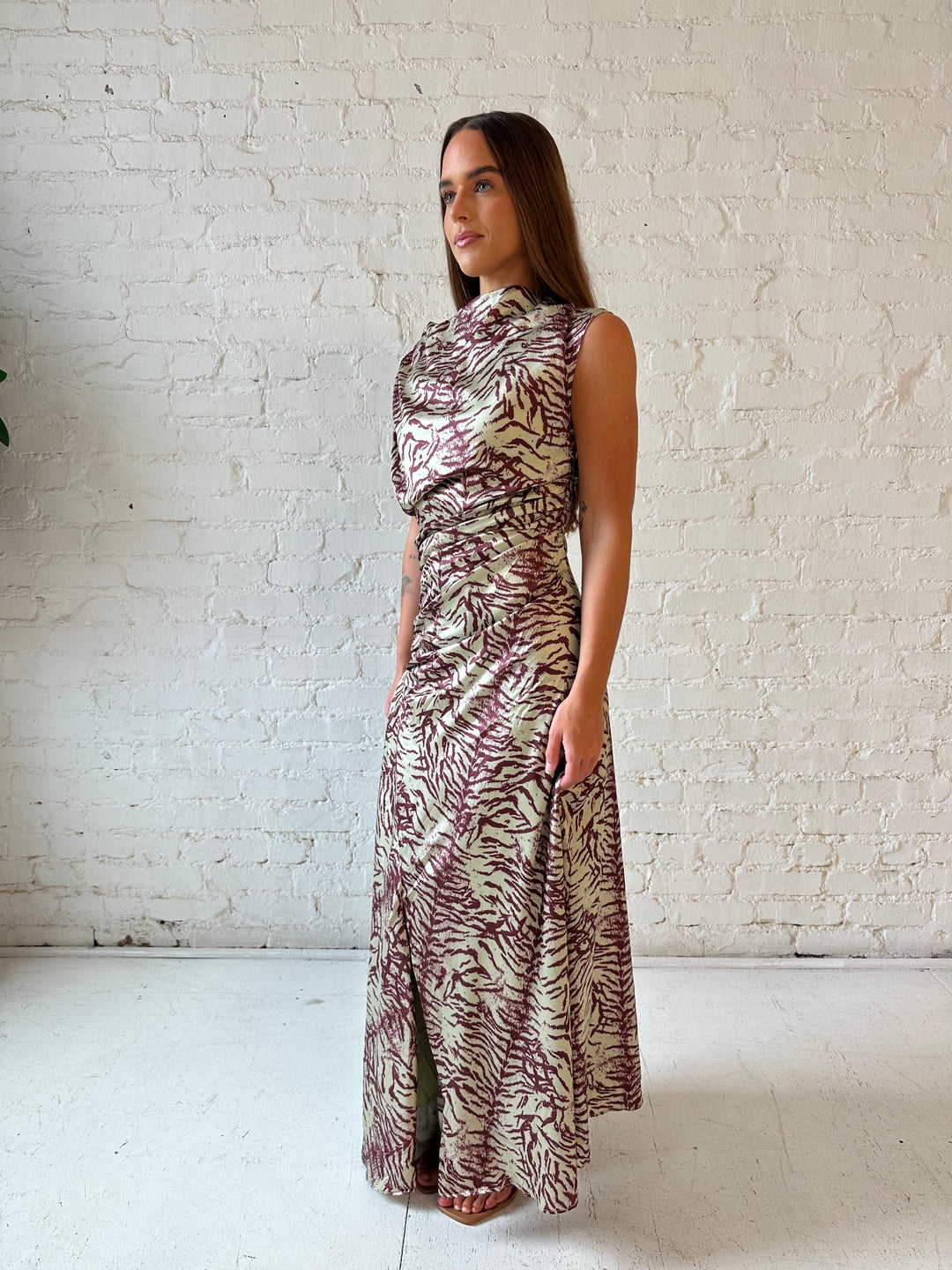 Woman wearing olive green animal print satin maxi dress with a high neckline, and side slit. 