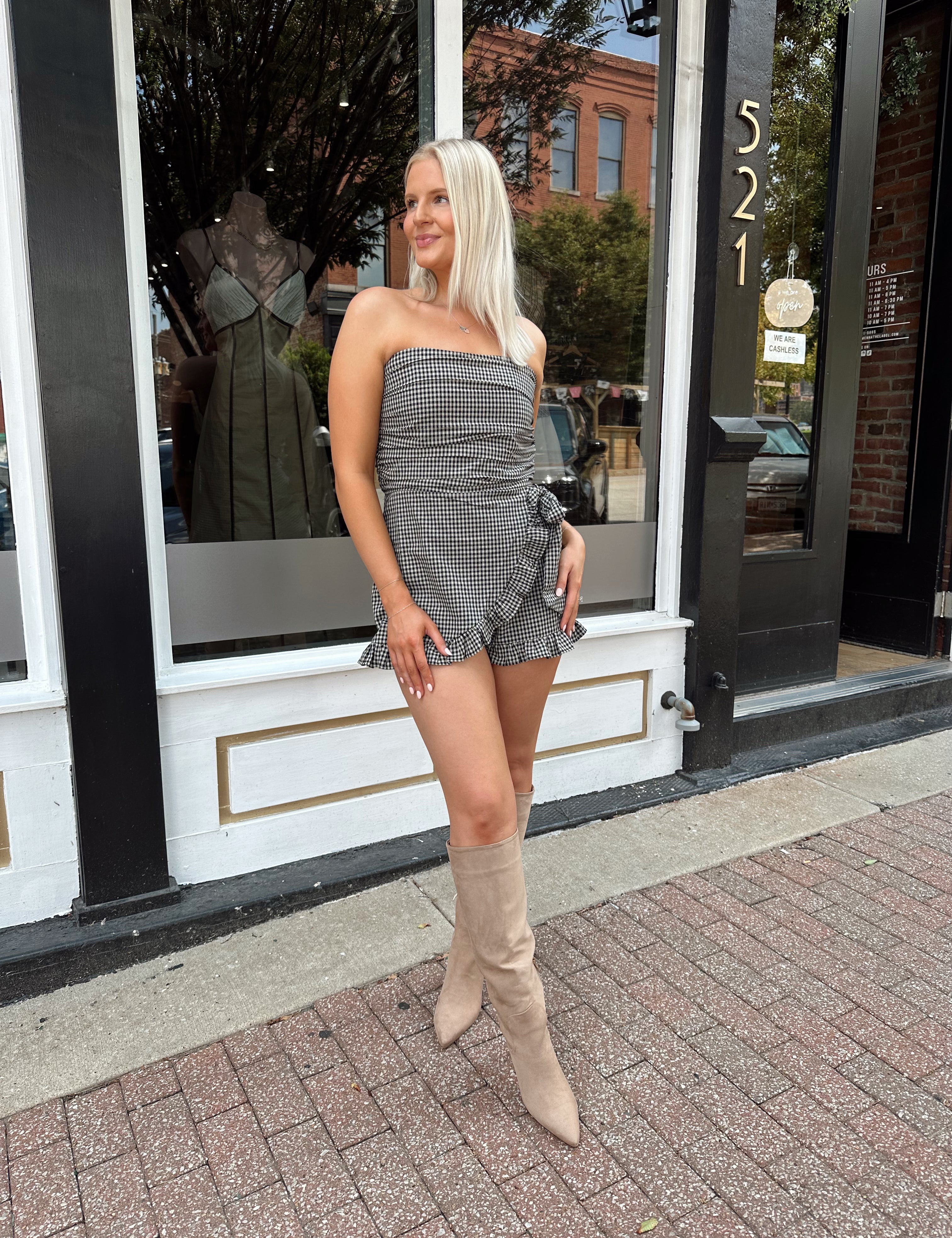 Woman wearing a black and taupe gingham strapless romper with wrap skirt. 