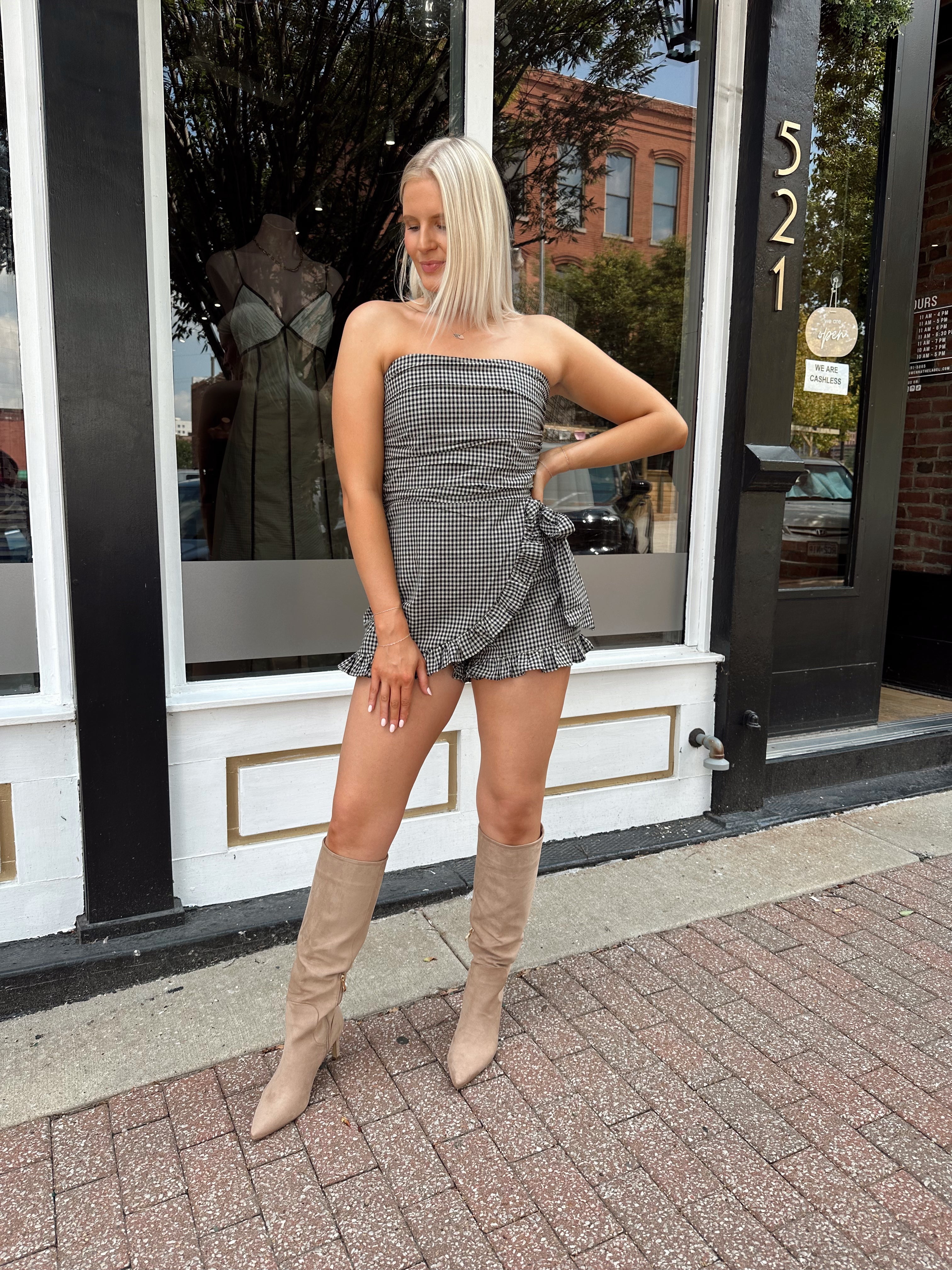 Woman wearing a black and taupe gingham strapless romper with wrap skirt. 