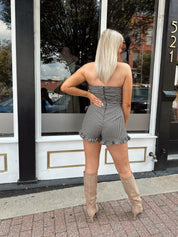 Woman wearing a black and taupe gingham strapless romper with wrap skirt. 