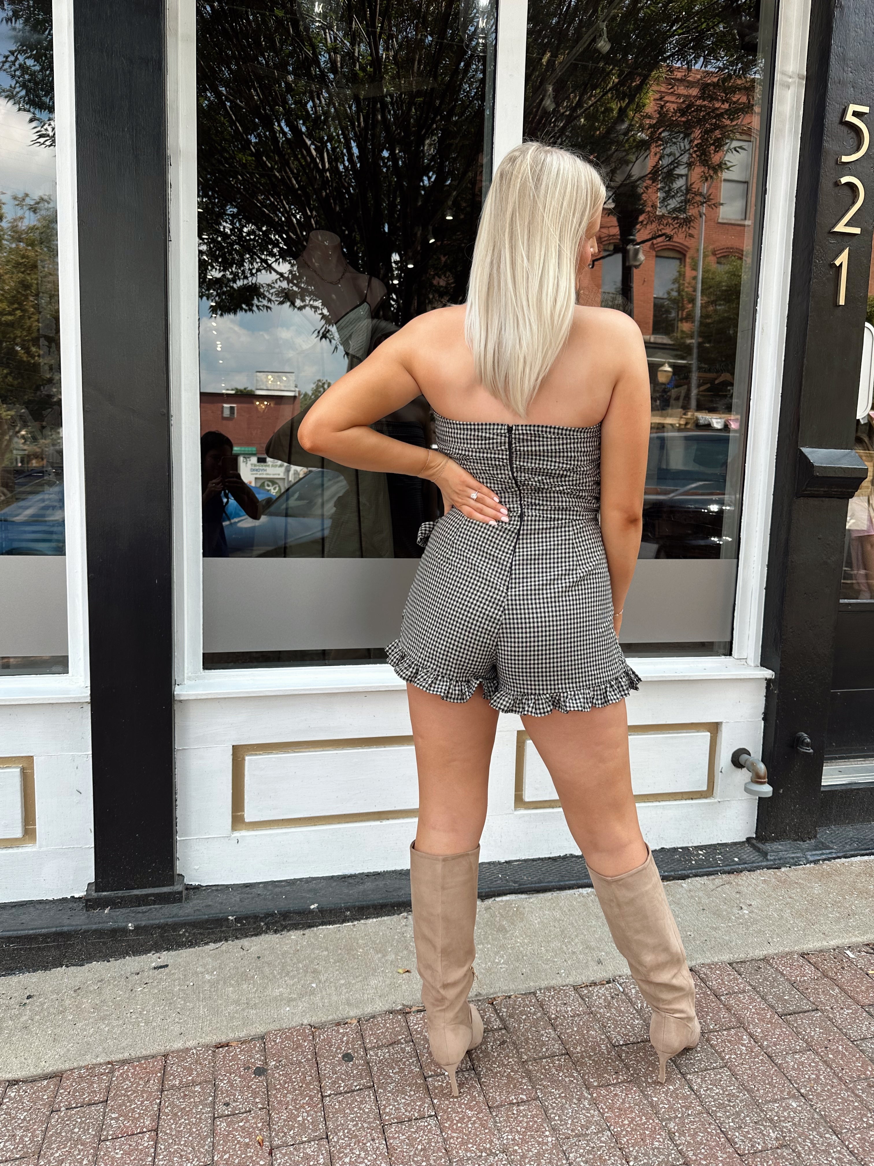 Woman wearing a black and taupe gingham strapless romper with wrap skirt. 