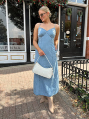 Woman wearing light wash denim midi dress with ivory lace embroidery detail and functional pockets.