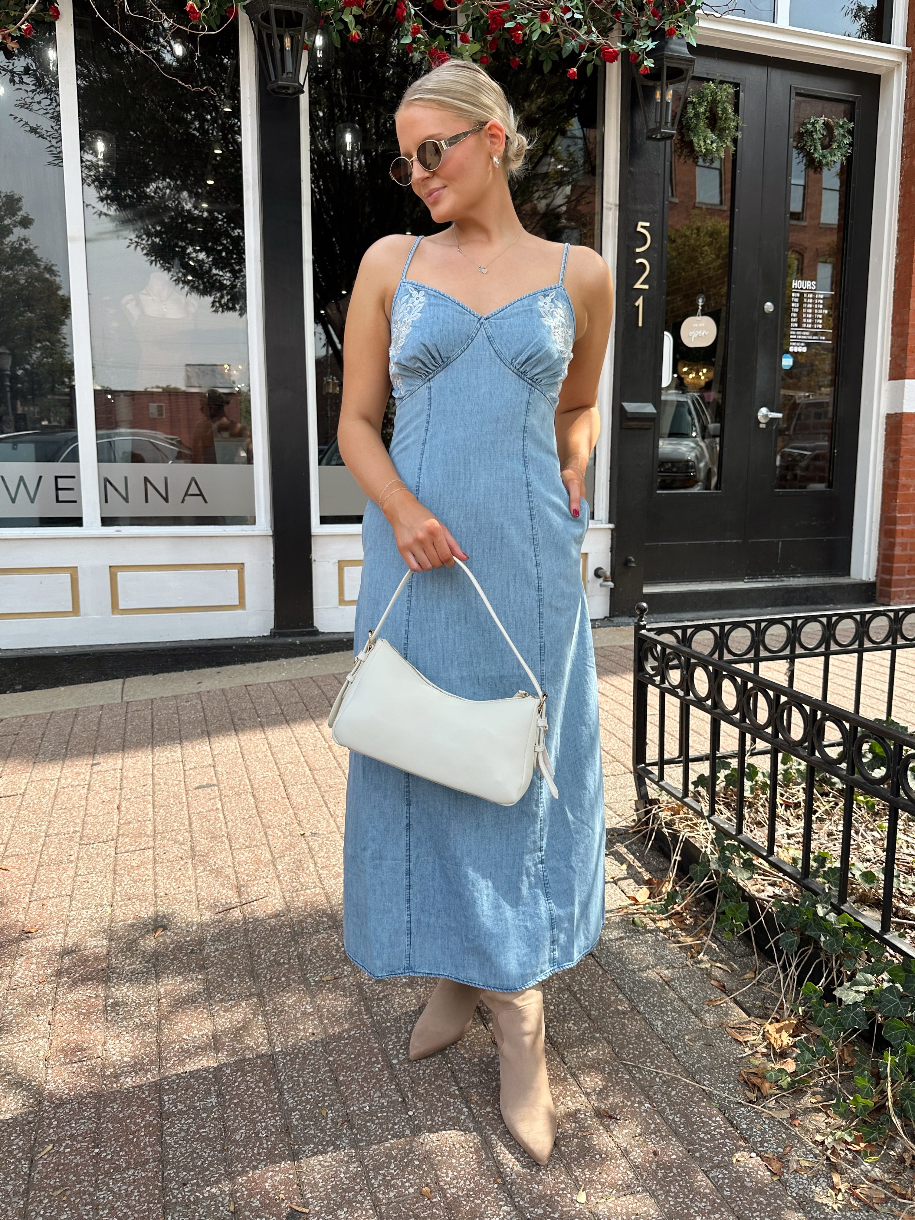 Woman wearing light wash denim midi dress with ivory lace embroidery detail and functional pockets.