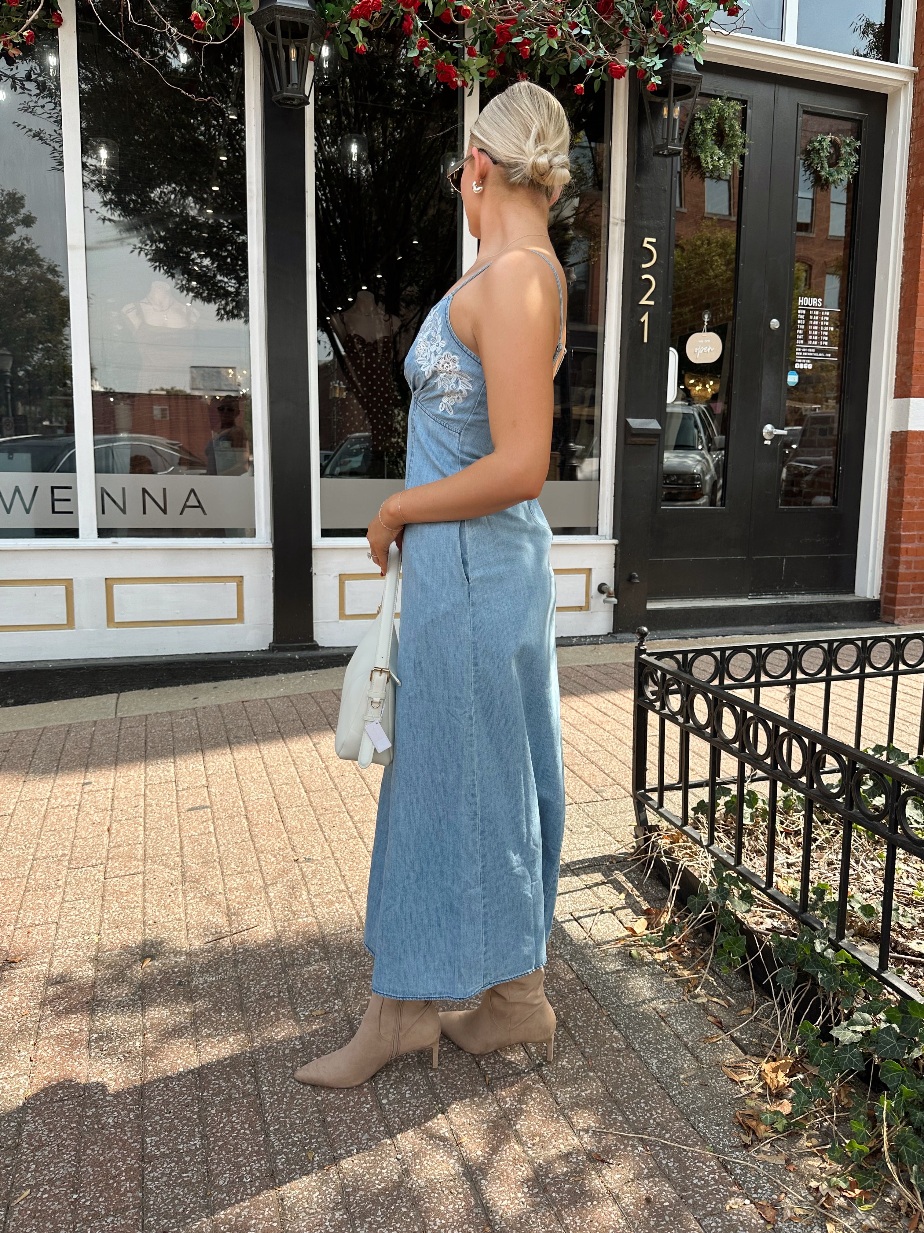 Woman wearing light wash denim midi dress with ivory lace embroidery detail and functional pockets.