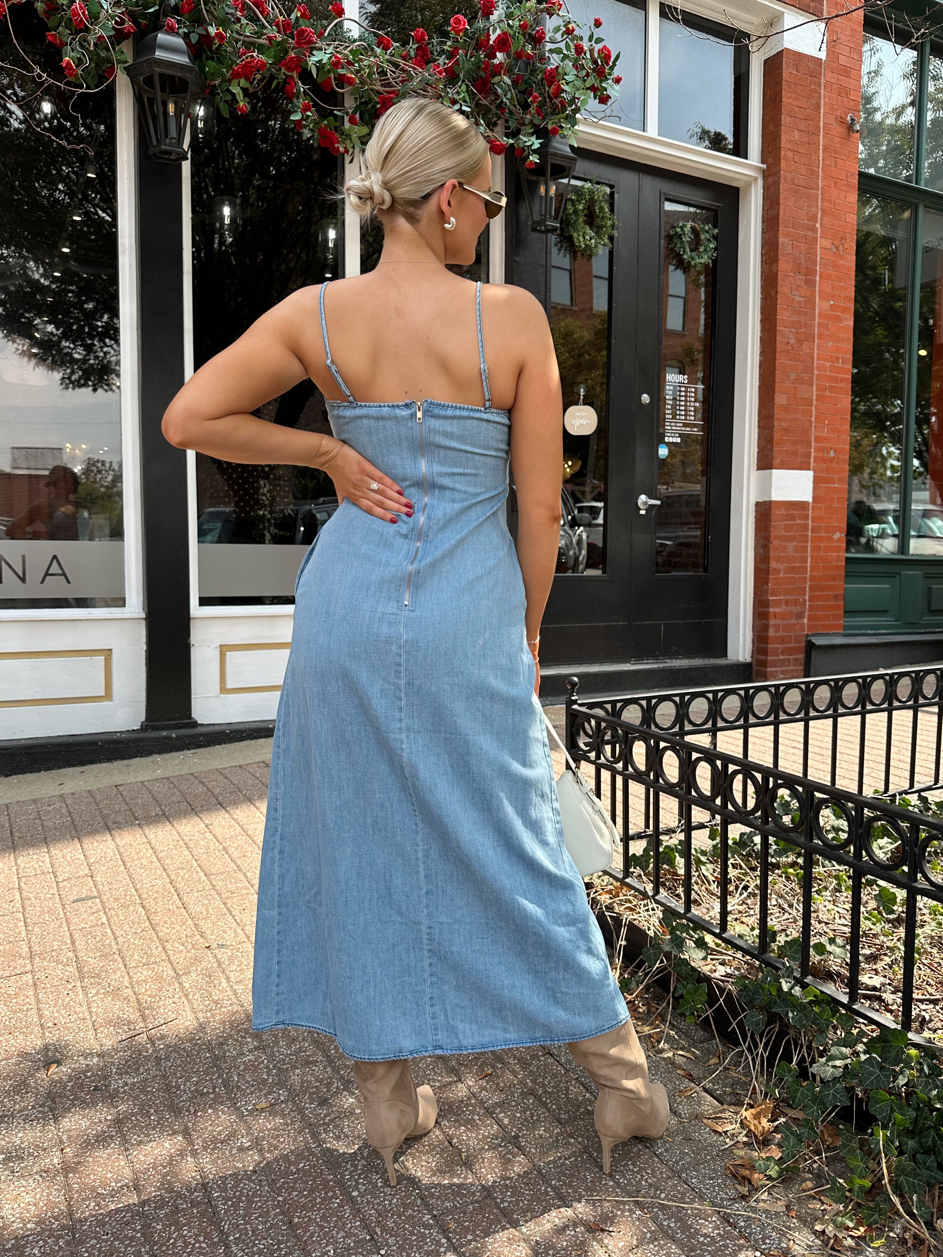 Woman wearing light wash denim midi dress with ivory lace embroidery detail and functional pockets.
