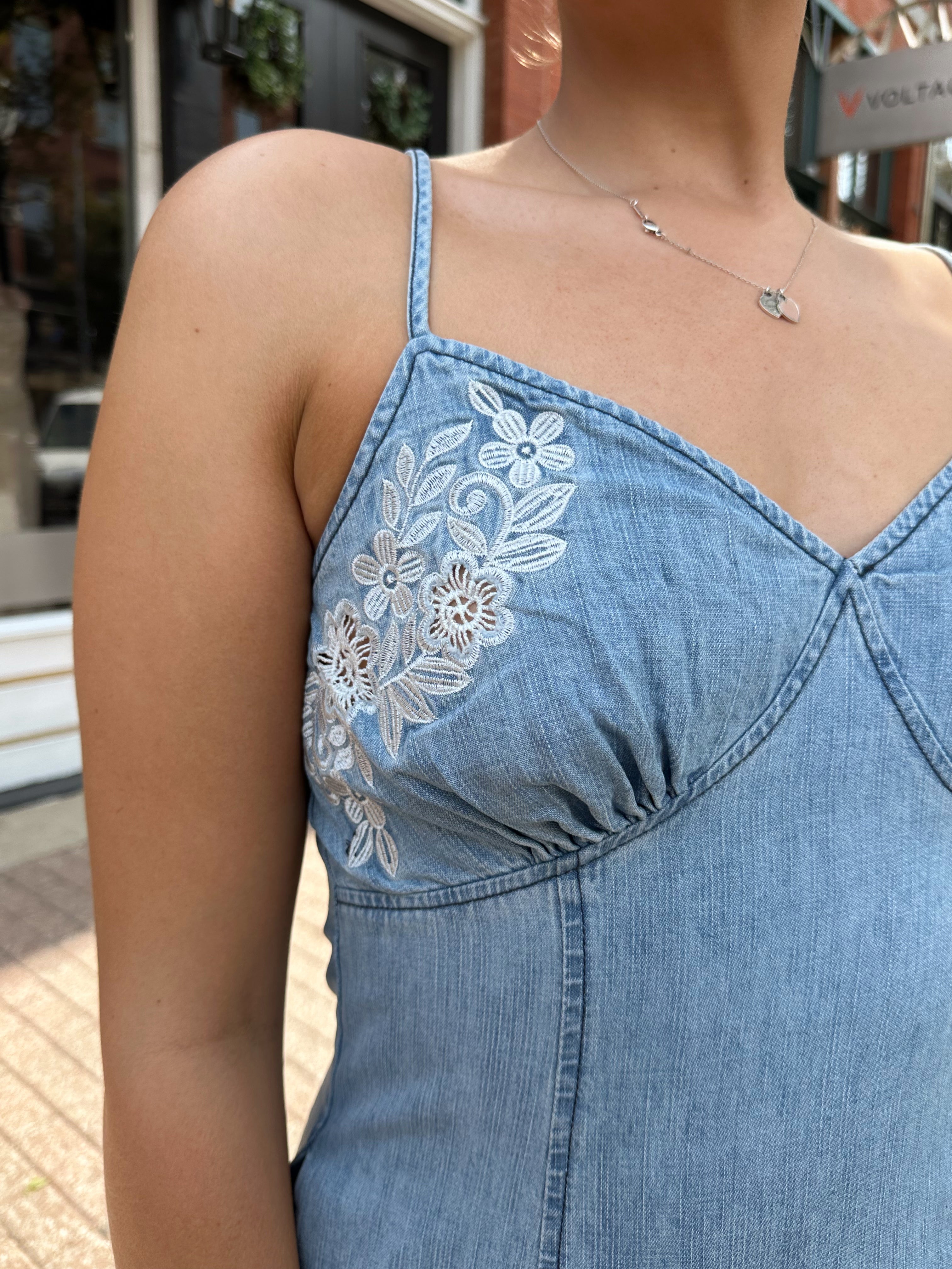 Woman wearing light wash denim midi dress with ivory lace embroidery detail and functional pockets.