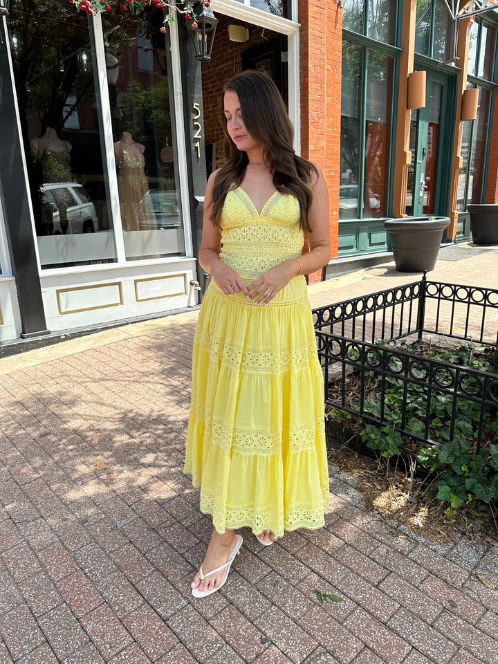 Woman wearing yellow textured maxi dress with v-neckline, adjustable straps and a tiered bottom. 