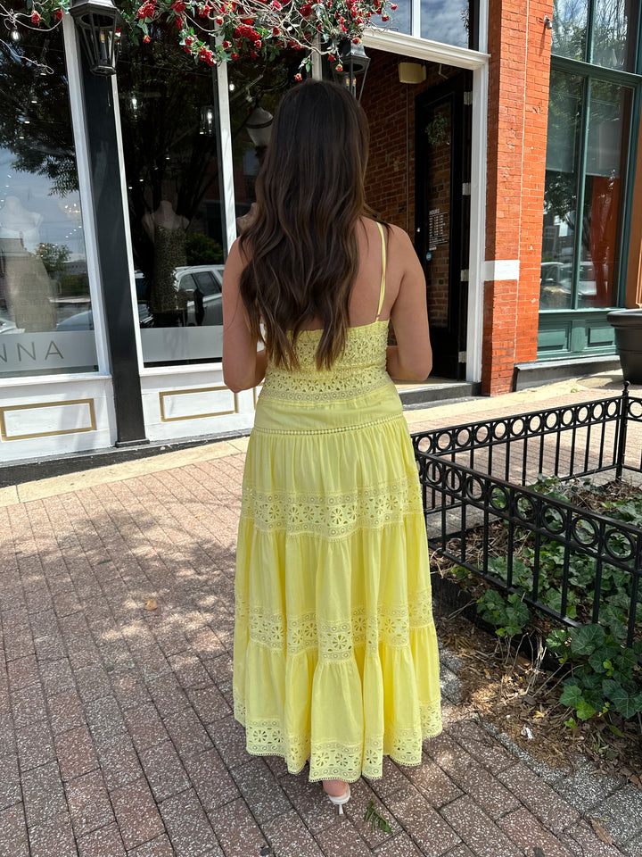 Woman wearing yellow textured maxi dress with v-neckline, adjustable straps and a tiered bottom. 