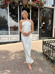 Woman wearing off white satin maxi dress with lace trim detailing, and self tie halter neck. 