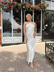 Woman wearing off white satin maxi dress with lace trim detailing, and self tie halter neck. 
