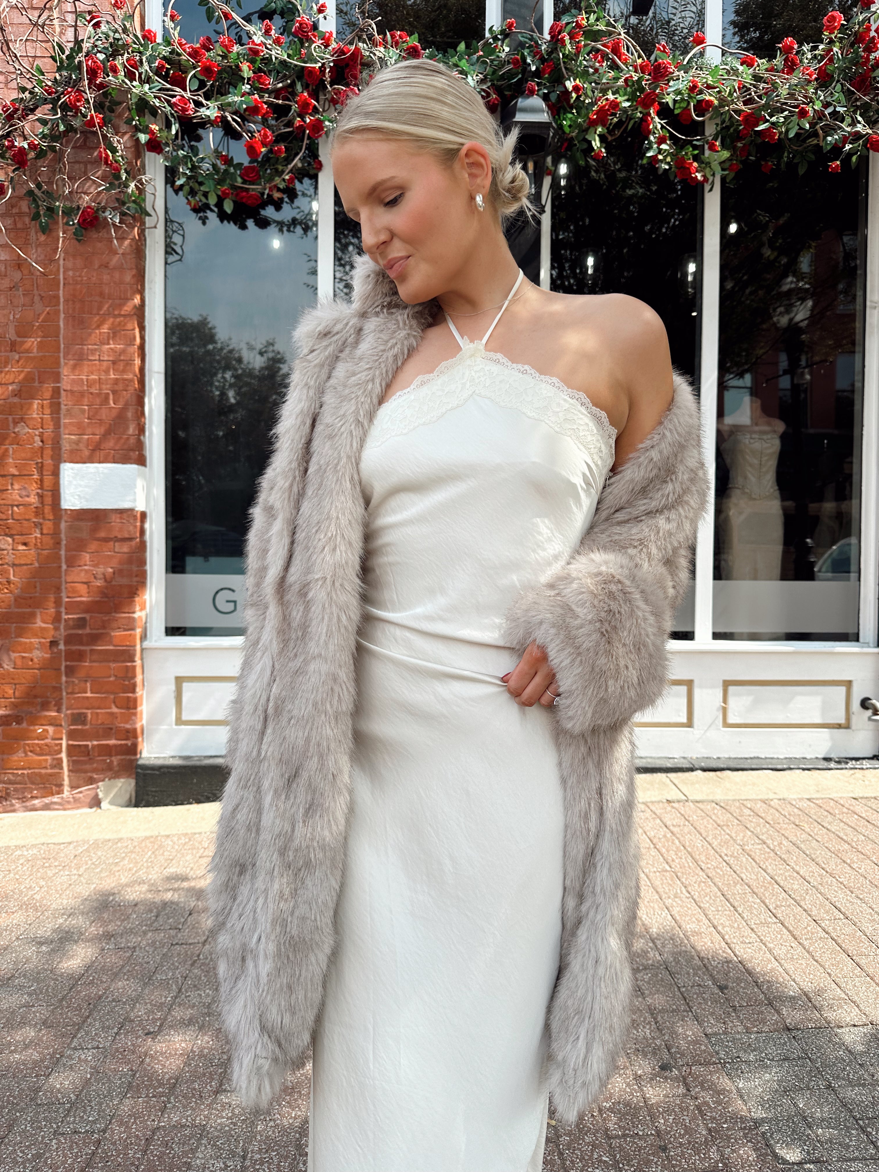 Woman wearing off white satin maxi dress with lace trim detailing, and self tie halter neck. 