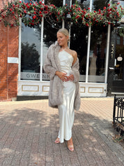 Woman wearing off white satin maxi dress with lace trim detailing, and self tie halter neck. 