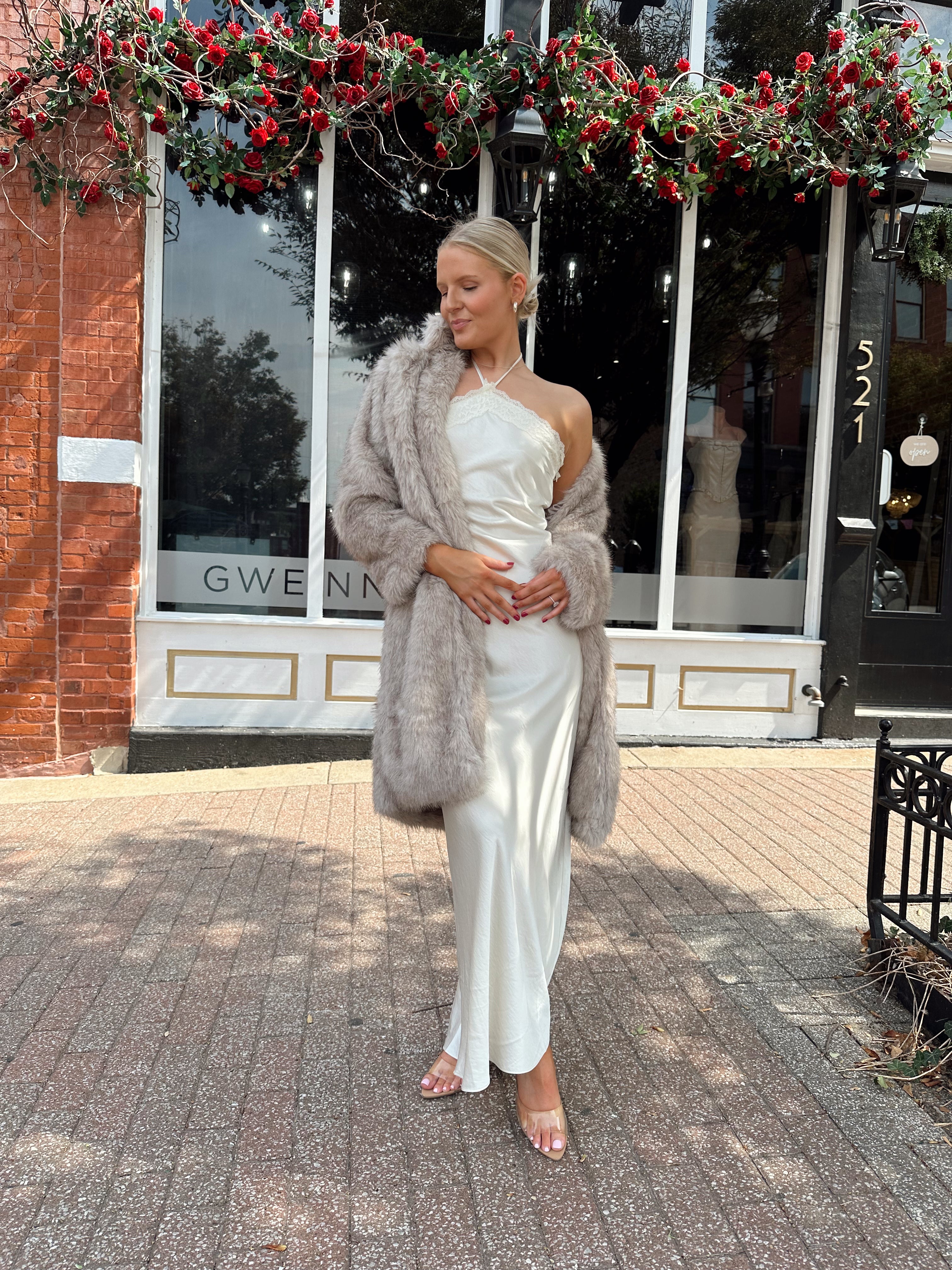 Woman wearing off white satin maxi dress with lace trim detailing, and self tie halter neck. 