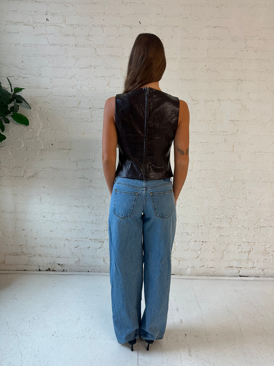 Woman wearing dark brown croc faux leather, high neck top, with medium wash jeans. 