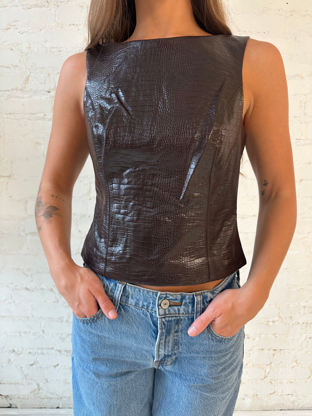 Woman wearing dark brown croc faux leather, high neck top, with medium wash jeans. 