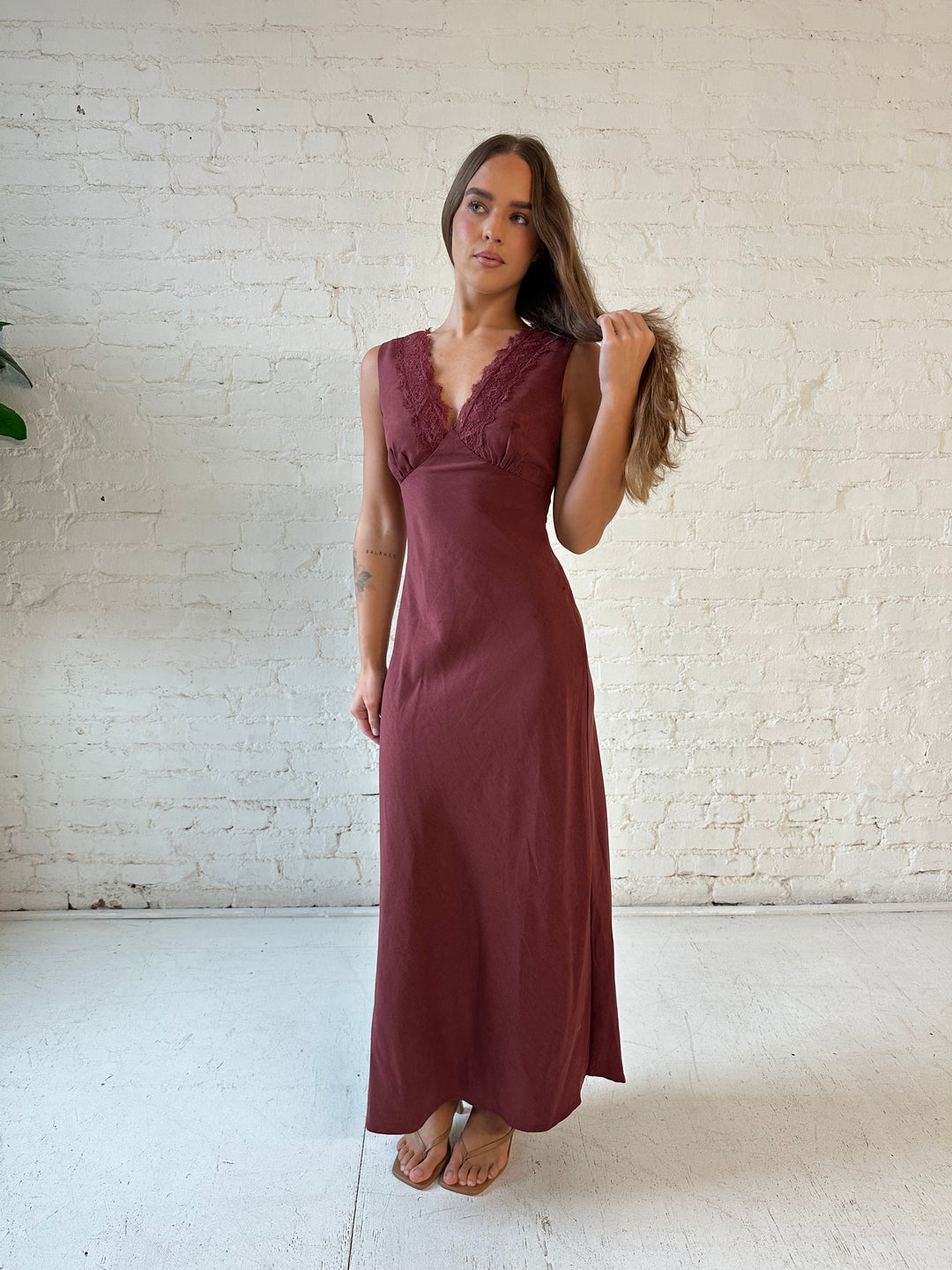 Woman wearing mahogany midi dress with v-neckline and lace trim detail with tie back.