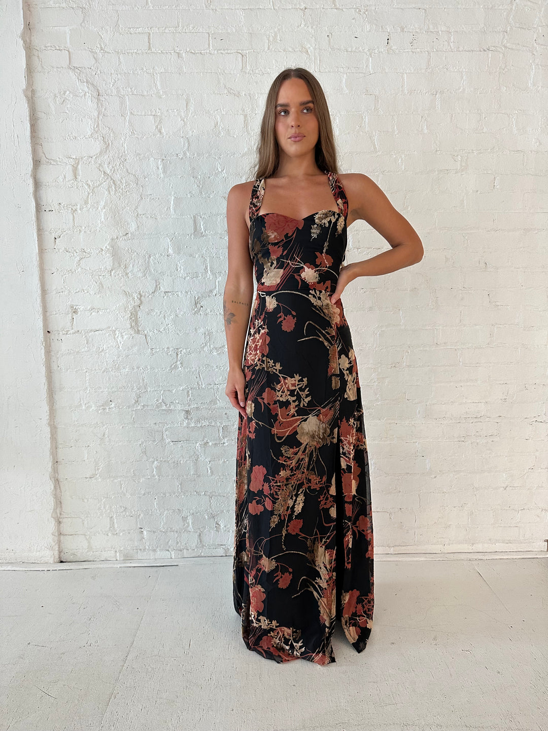 Woman wearing floral velvet maxi dress with side slit, and open lace up back.