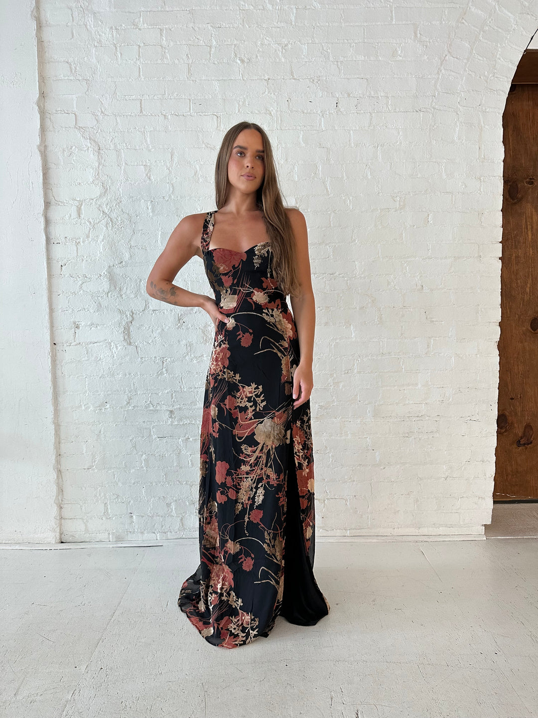 Woman wearing floral velvet maxi dress with side slit, and open lace up back.