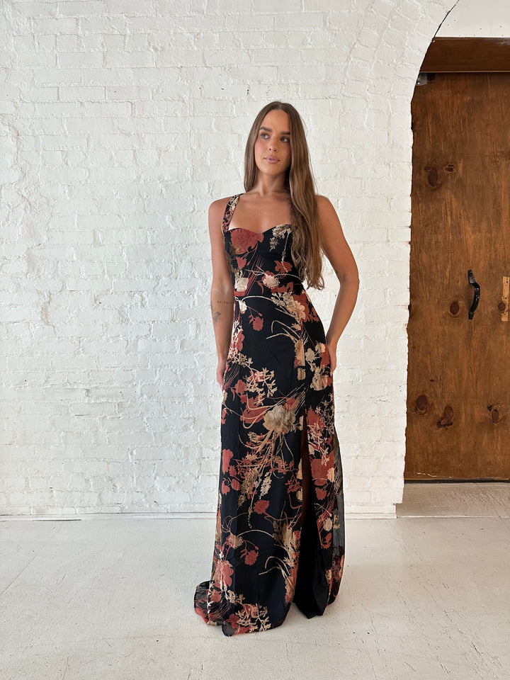 Woman wearing floral velvet maxi dress with side slit, and open lace up back.