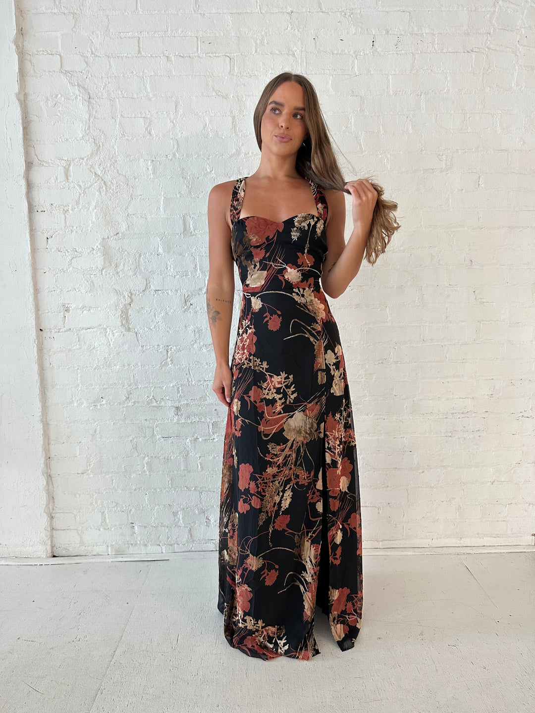 Woman wearing floral velvet maxi dress with side slit, and open lace up back.