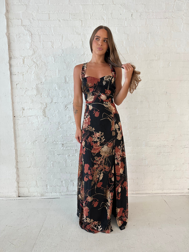 Woman wearing floral velvet maxi dress with side slit, and open lace up back.