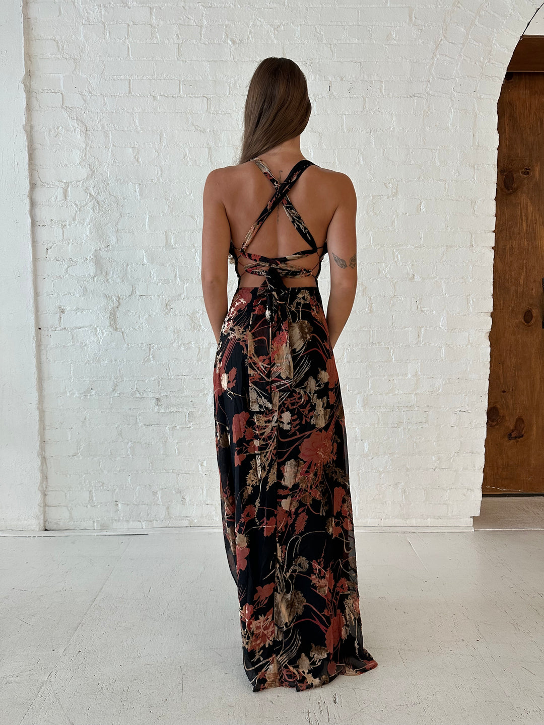 Woman wearing floral velvet maxi dress with side slit, and open lace up back.