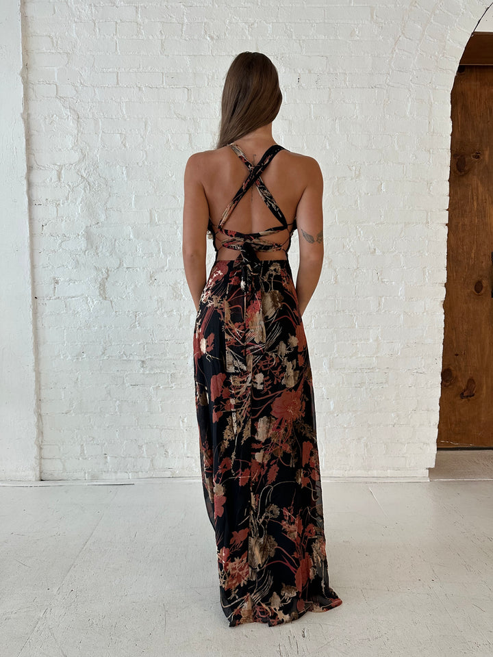 Woman wearing floral velvet maxi dress with side slit, and open lace up back.