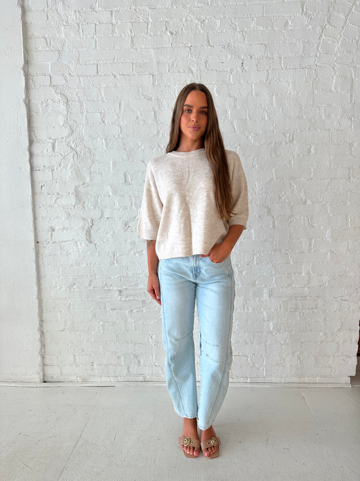 Woman wearing oatmeal knit relaxed fit top with light wash barrel jean.