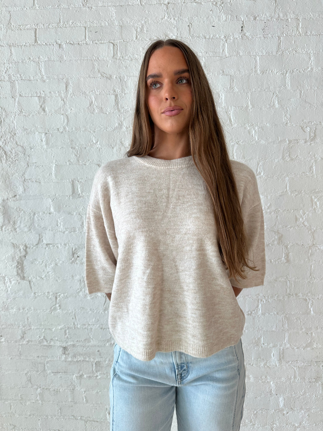 Woman wearing oatmeal knit relaxed fit top with light wash barrel jean.