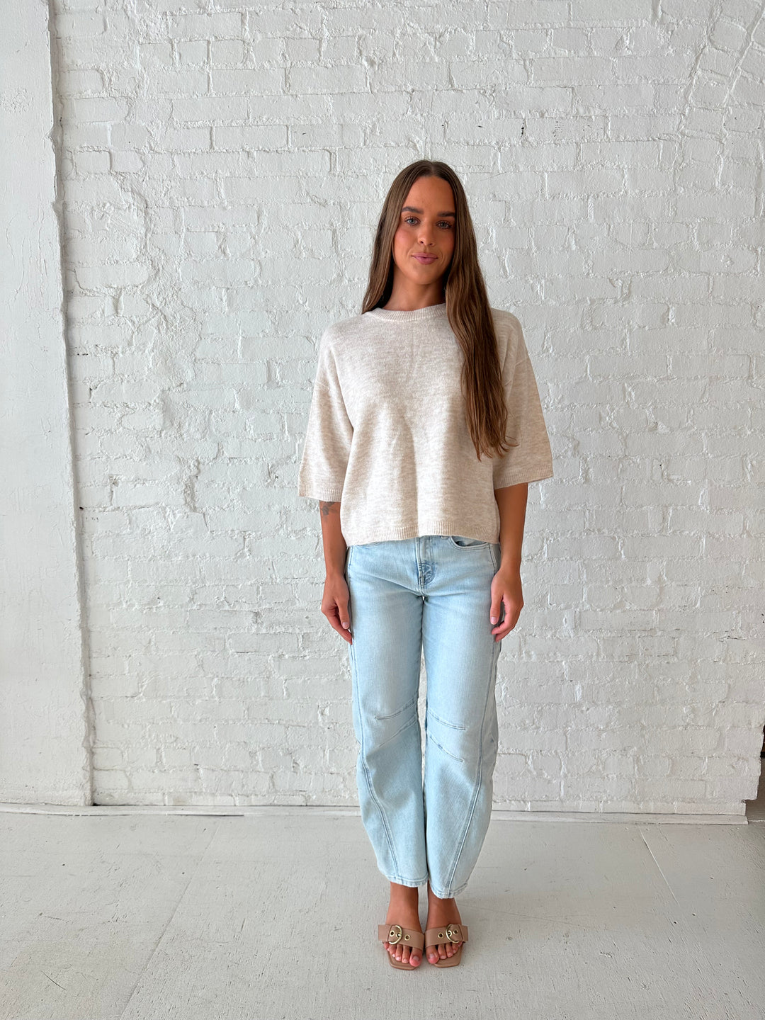 Woman wearing oatmeal knit relaxed fit top with light wash barrel jean.