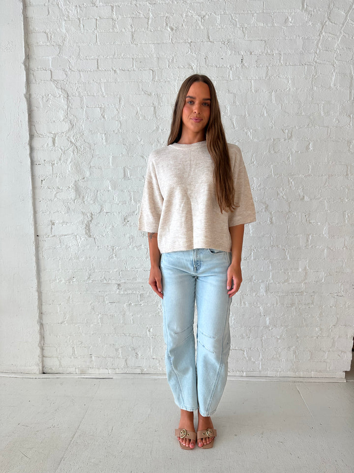 Woman wearing oatmeal knit relaxed fit top with light wash barrel jean.