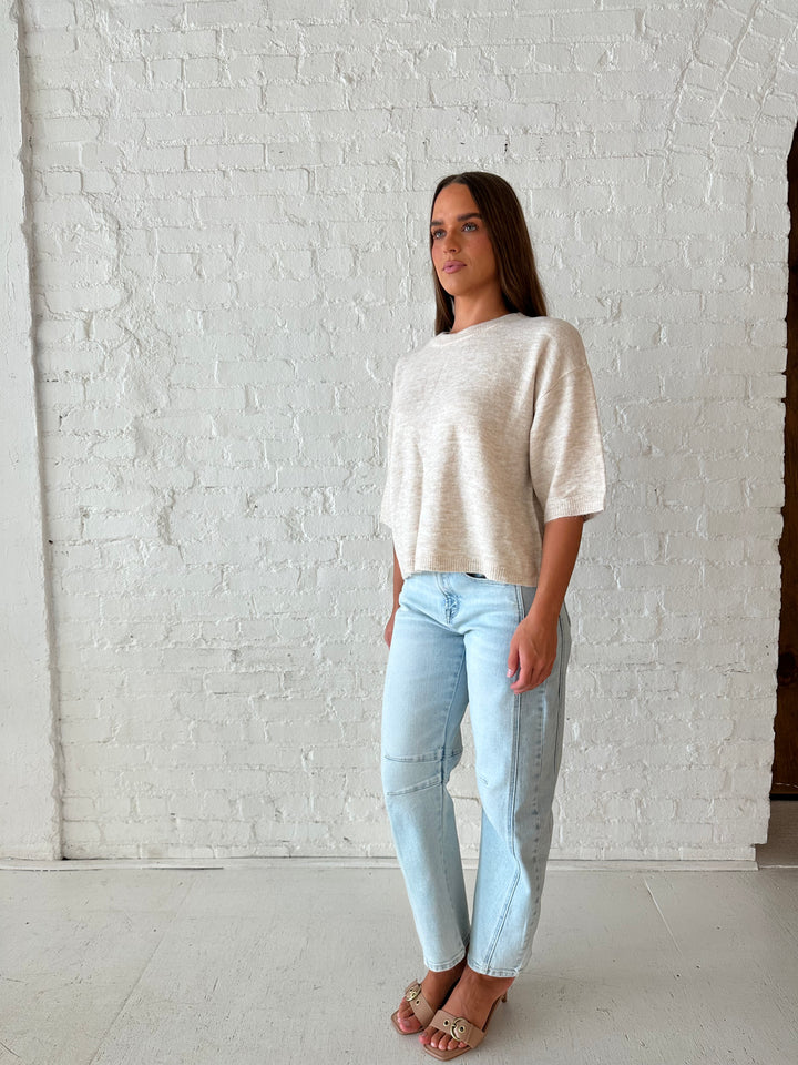 Woman wearing oatmeal knit relaxed fit top with light wash barrel jean.