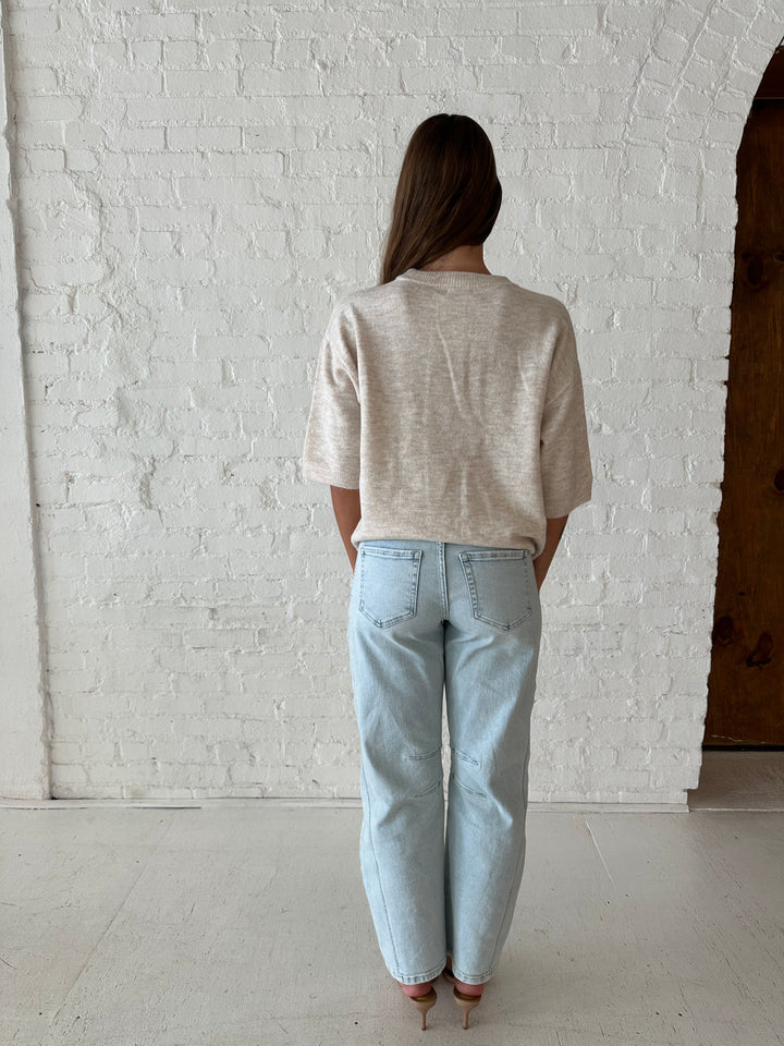 Woman wearing oatmeal knit relaxed fit top with light wash barrel jean.