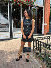 Woman wearing black leather mini dress with button detailing, belt loops, and functional pockets.