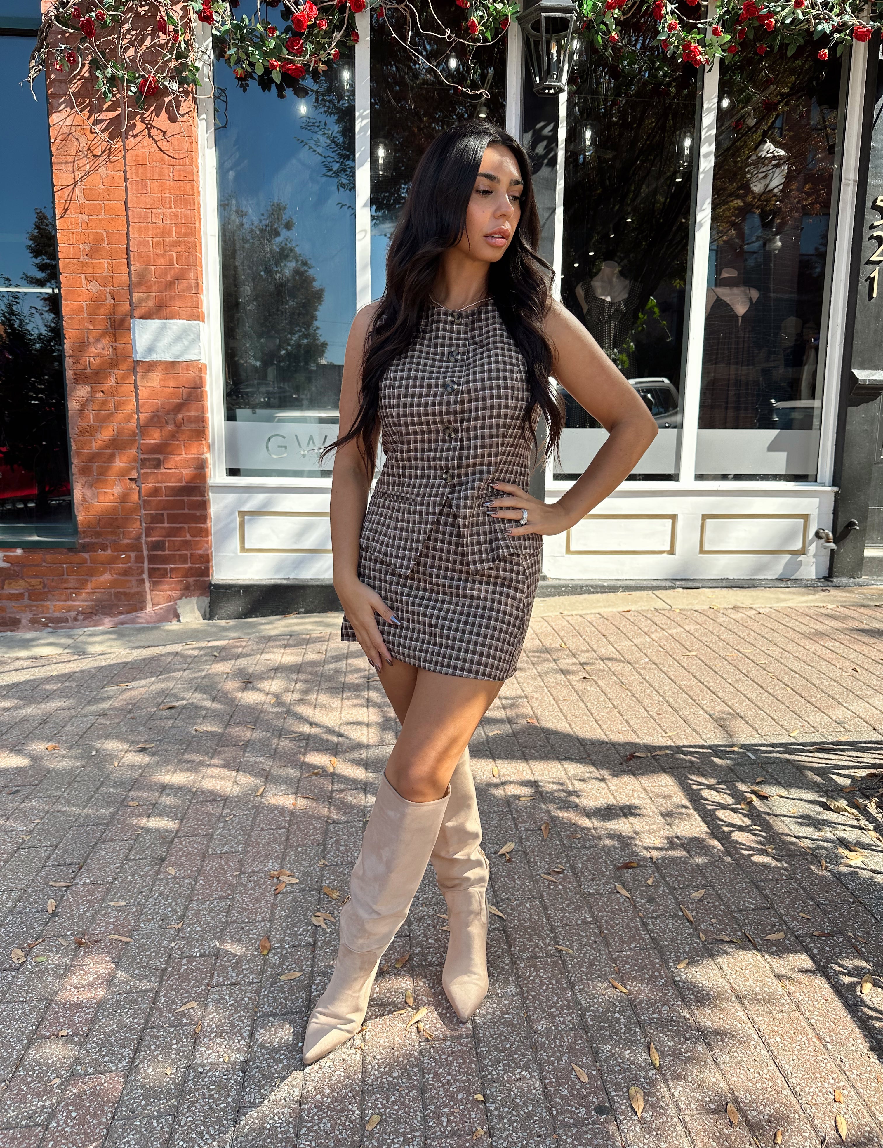 Woman wearing brown plaid two piece set with button down top and mini skirt. 
