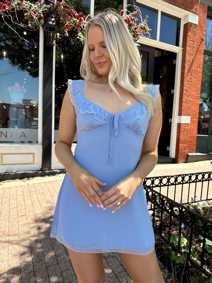 Woman wearing blue chiffon slip dress with trim detailing and adjustable straps.