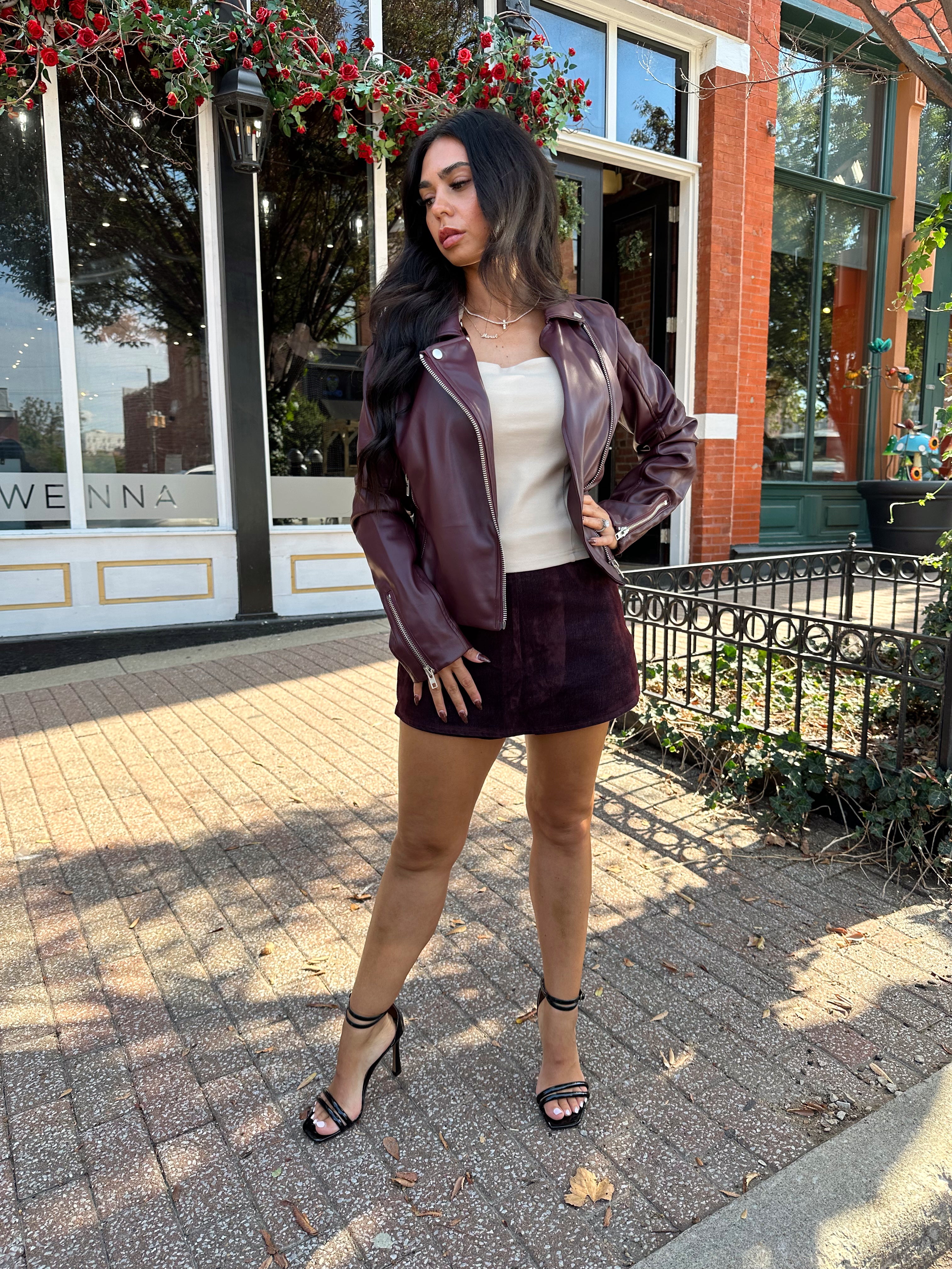Woman wearing burgundy matte leather jacket with burgundy mini skort. 