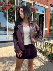 Woman wearing burgundy matte leather jacket with burgundy mini skort. 