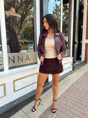 Woman wearing burgundy matte leather jacket with burgundy mini skort. 