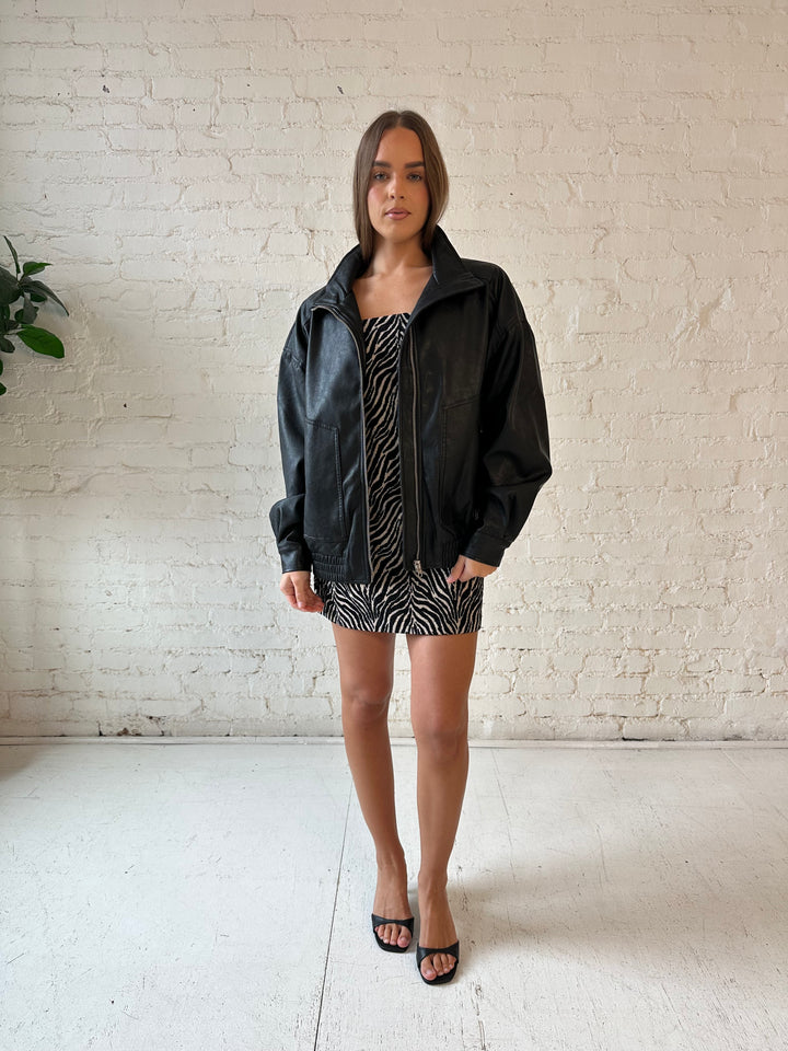 Woman wearing oversized black faux leather jacket with animal print mini dress.