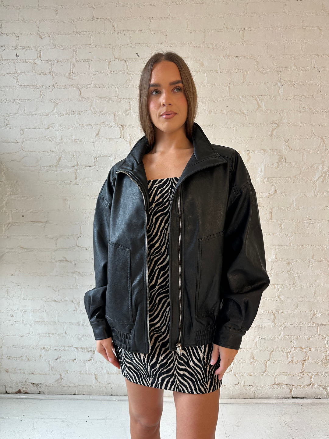 Woman wearing oversized black faux leather jacket with animal print mini dress.